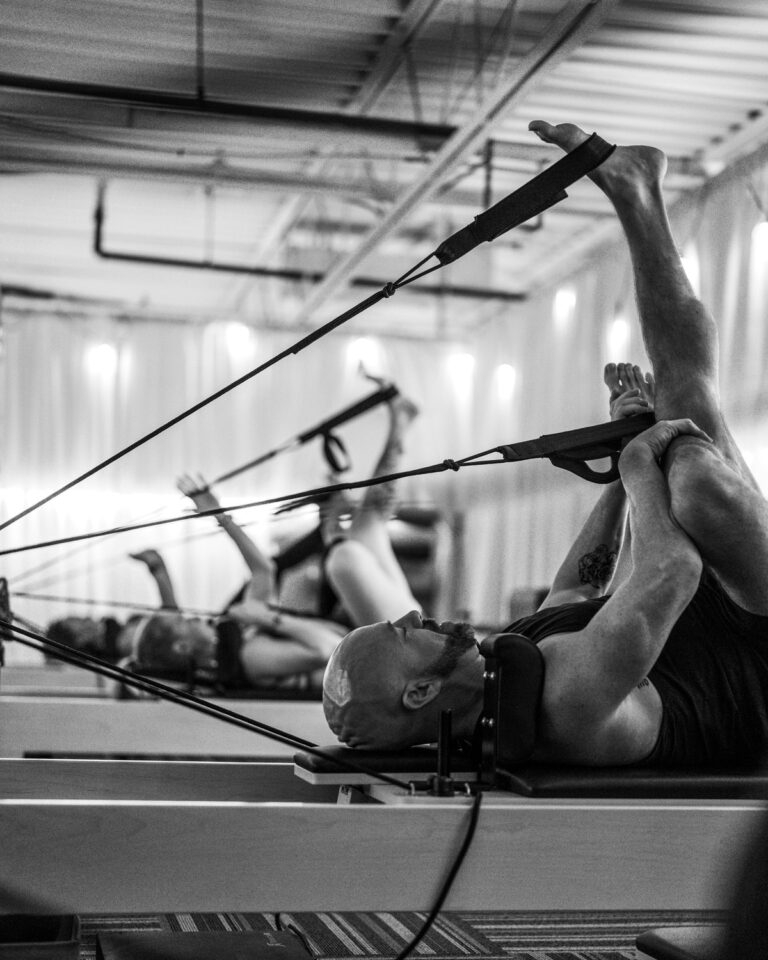 A member lying back on a reformer with both feet in the straps