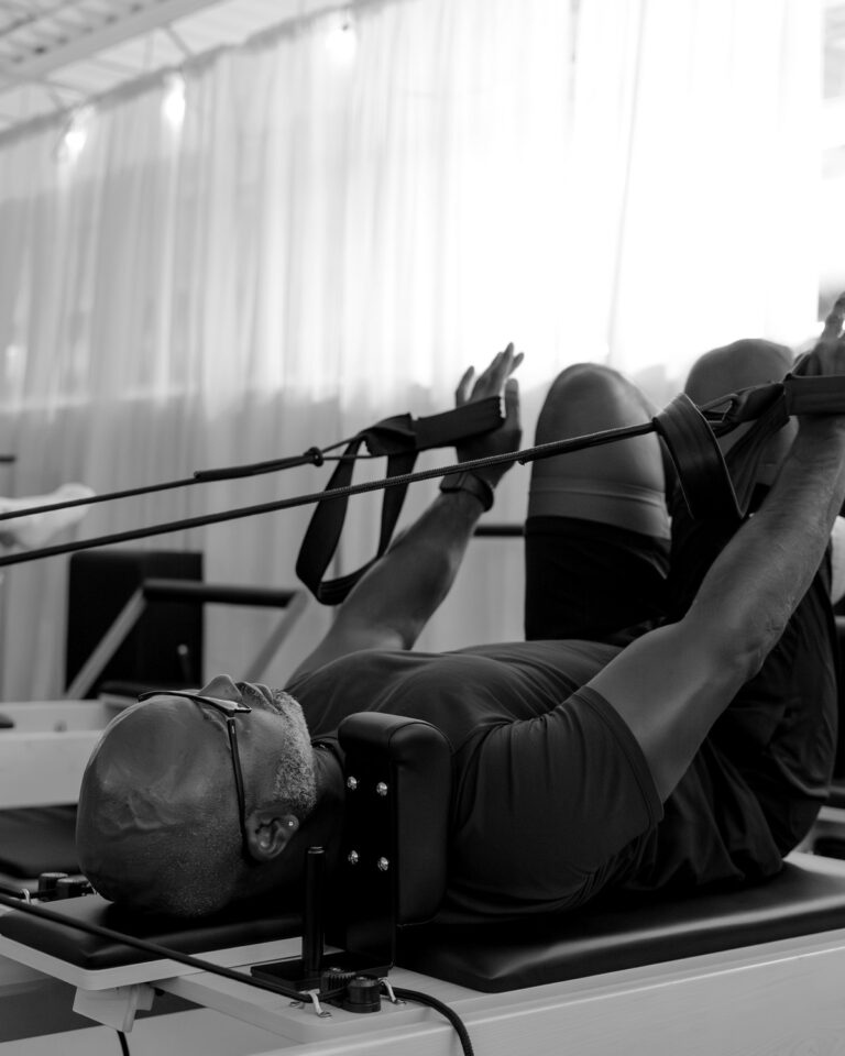 A member lying on a reformer with arms extended in the straps